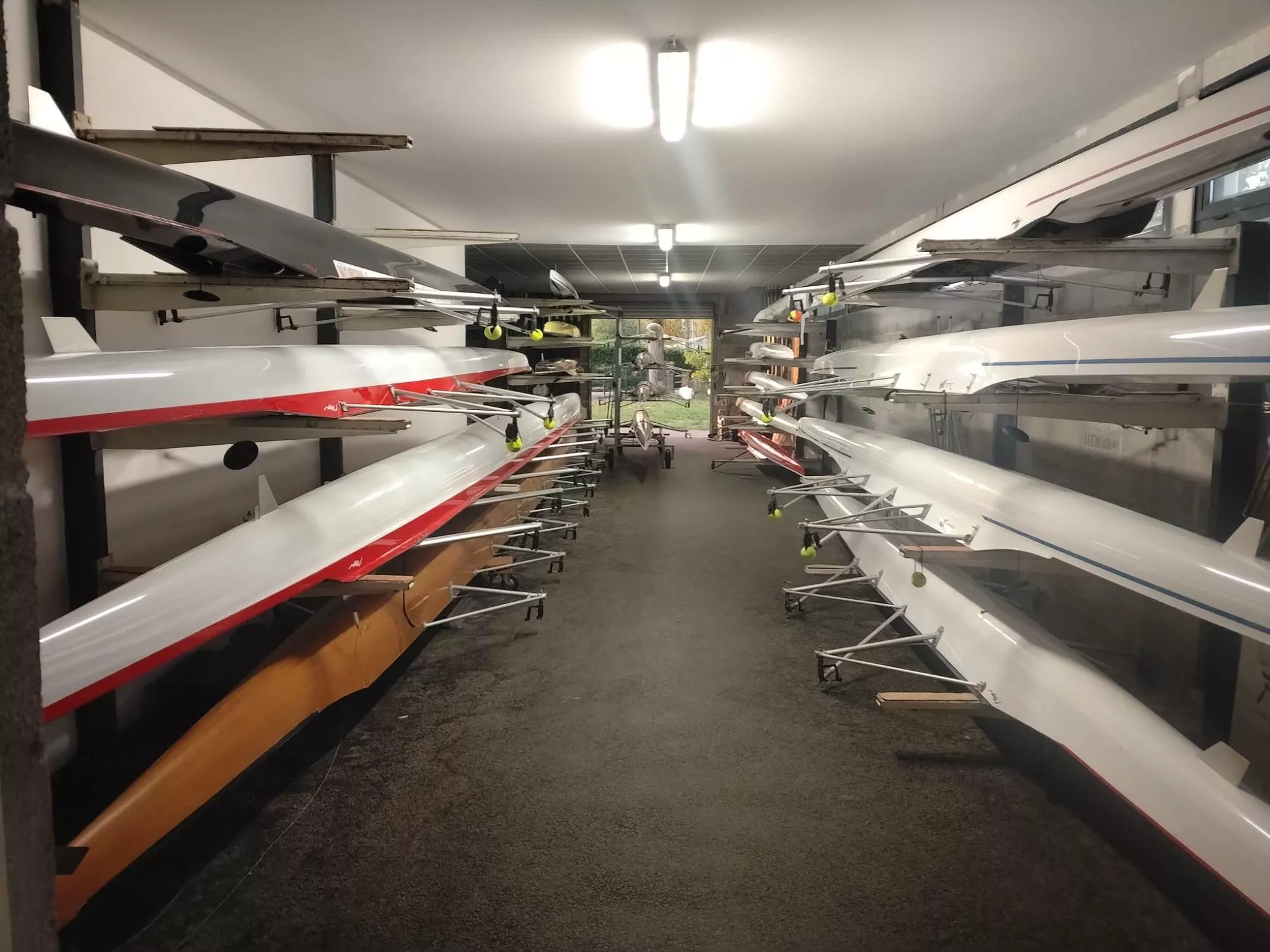 Skiffs et bateaux d'équipe rangés sur les racks du garage à bateaux de l'Aviron Club Moissac