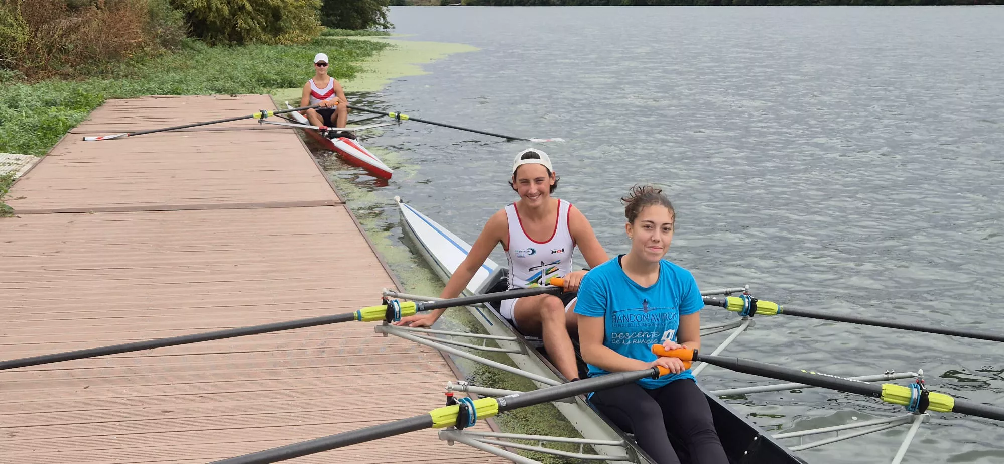 Trois rameurs souriants au ponton, prêts à partir en deux de couple et en skiff
