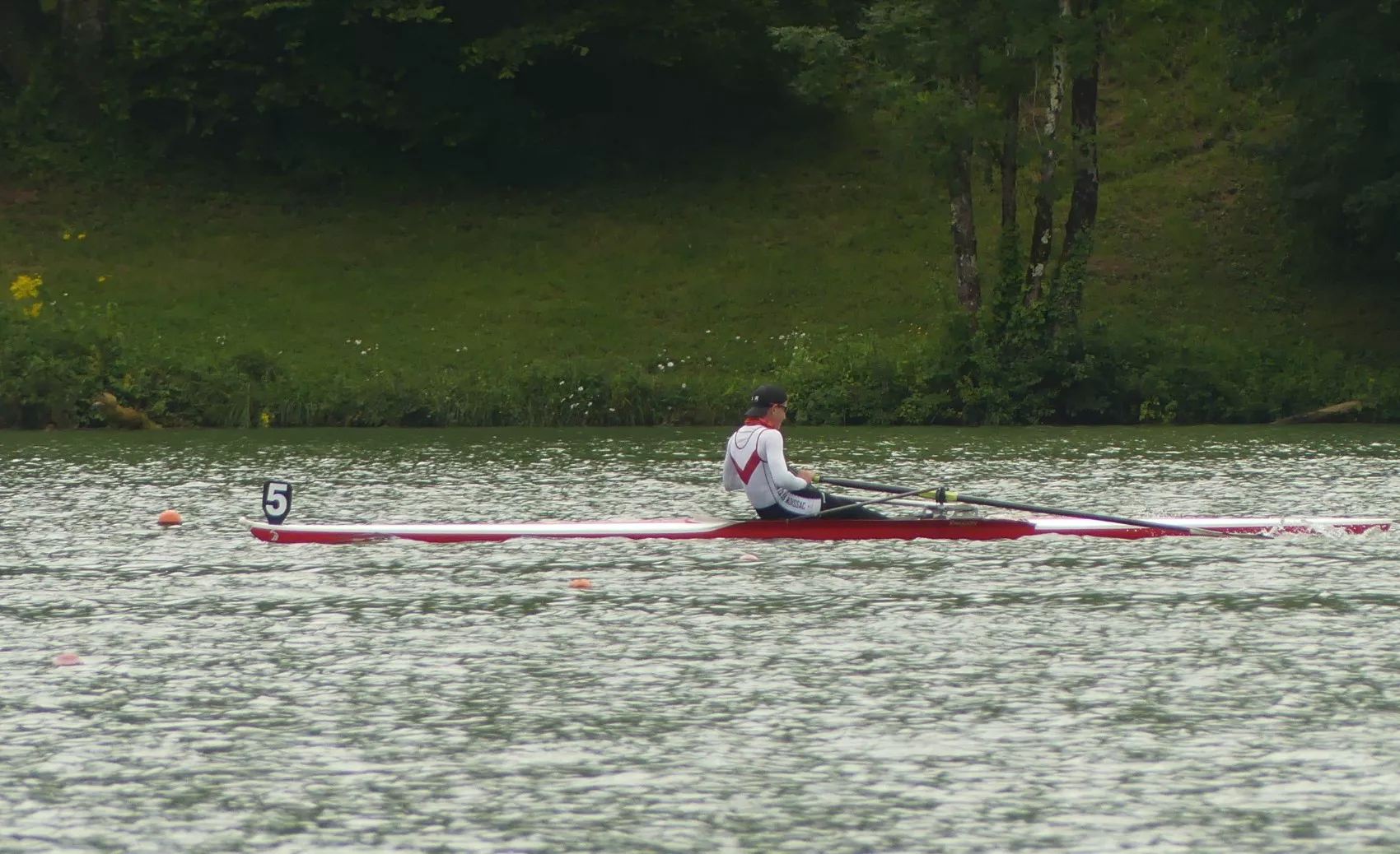 Un rameur de l'Aviron Club Moissac en skiff rouge sur un bassin de régate, à la ligne 5